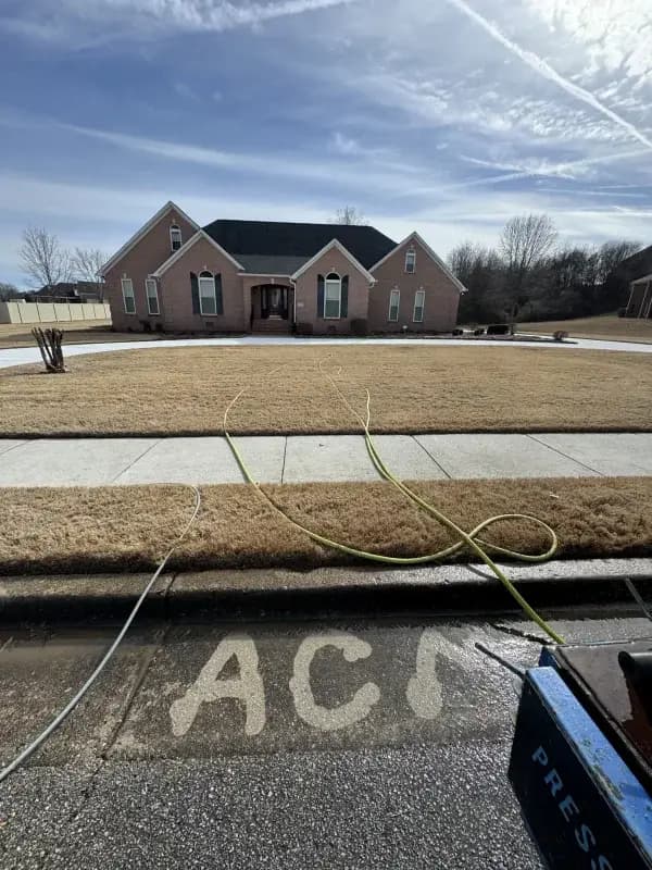 A freshly cleaned street apron in front of a brick home, with ACM written in the cleaned concrete